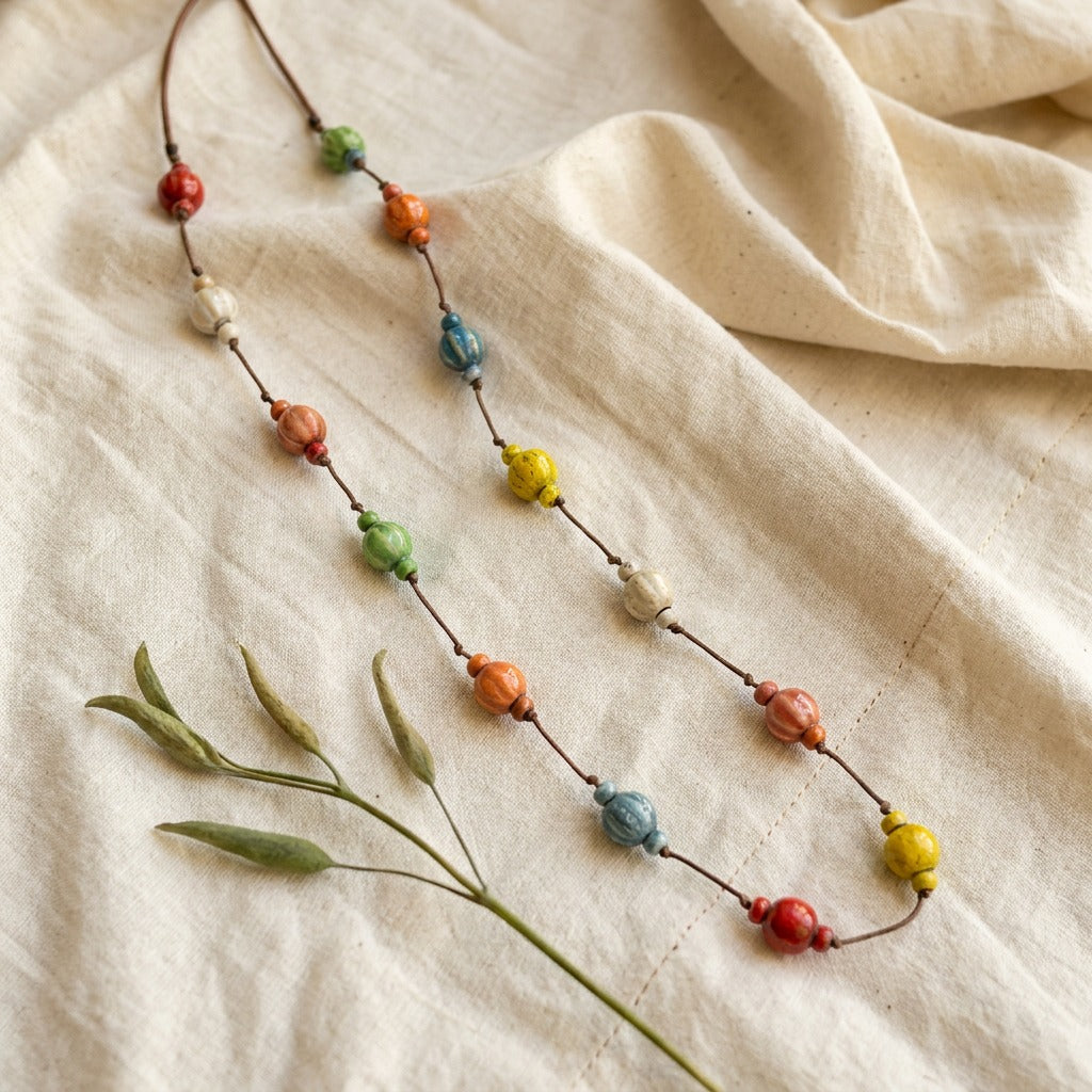 A playful rhythm of earthy colors and handmade charm, this necklace features scattered ceramic-style beads arranged along a natural cord for an artistic boho look. Its warm tones and free-flowing design create a relaxed statement that feels colorful, soulful, and effortlessly unique.
