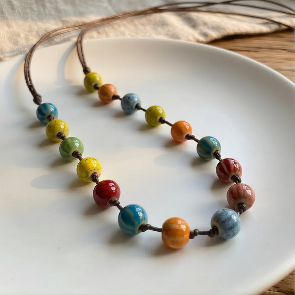A joyful blend of color, creativity, and handmade charm, this necklace features vibrant ceramic-style beads arranged along a natural cord to create a playful yet artistic statement. Its cheerful palette and free-spirited design bring warmth, personality, and effortless bohemian elegance to any look.
