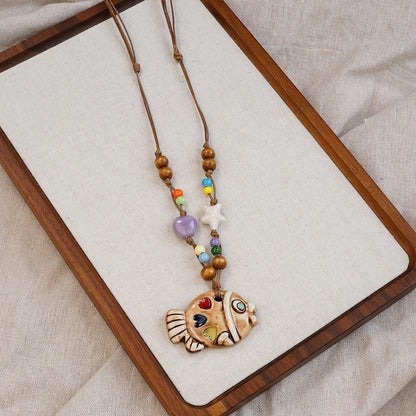 A playful blend of color and craftsmanship, this handmade fish pendant carries tiny heart details that feel full of warmth and personality. With its artistic ceramic finish and soft earthy tones, it brings a whimsical, story-like charm to your everyday look.