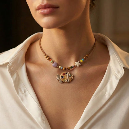 A playful blend of color and craftsmanship, this handmade fish pendant carries tiny heart details that feel full of warmth and personality. With its artistic ceramic finish and soft earthy tones, it brings a whimsical, story-like charm to your everyday look.