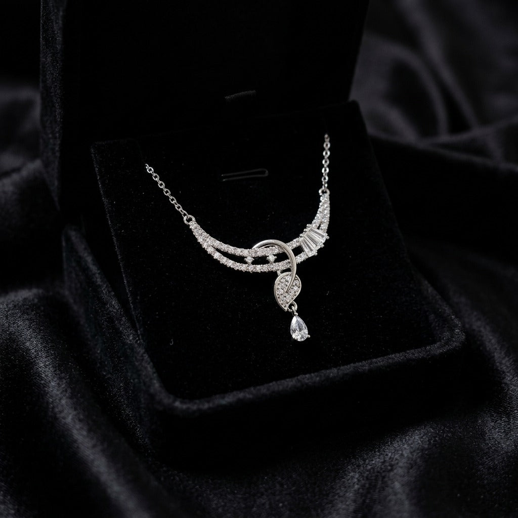 A flowing curve of shimmering crystals paired with a delicate heart drop, this necklace captures an elegant sparkle that feels graceful from every angle. The soft cascading design adds a refined charm that beautifully balances romance and modern luxury.
