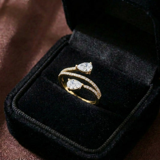 A graceful dance of symmetry and sparkle, this ring features two radiant pear-cut stones flowing toward each other in an elegant open-wrap silhouette. The curved pavé band creates a soft, modern brilliance that feels refined and effortlessly romantic.