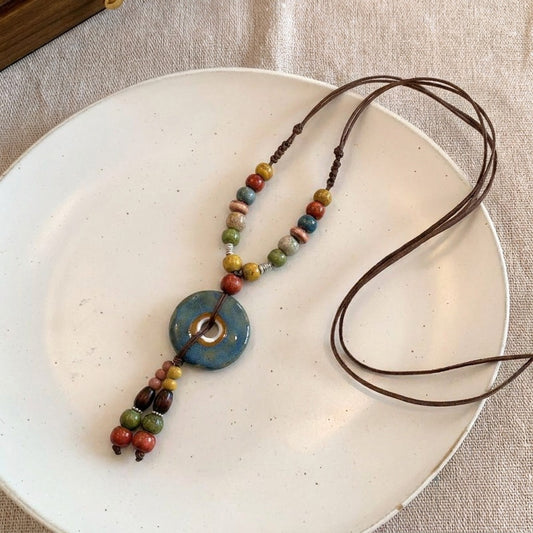 A harmony of earthy colors and handcrafted charm, this pendant blends rustic beads, natural tones, and a ceramic-inspired centerpiece into a design that feels calm, artistic, and free-spirited. Its boho silhouette carries the warmth of nature in every detail.