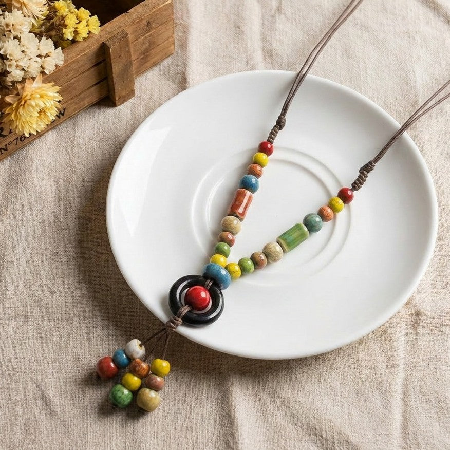 A playful circle of color and handmade charm, this necklace features vibrant ceramic-style beads paired with a bold loop centerpiece for an artistic boho statement. Its cheerful palette and free-spirited design bring a joyful touch to everyday styling.