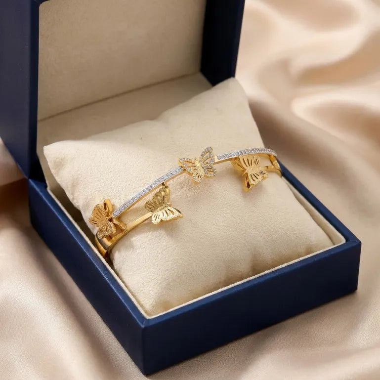 Delicate butterflies appear to dance across this elegant open cuff, creating a design that feels light, graceful, and full of charm. Accented with shimmering crystal details and a radiant gold-tone finish, this piece captures the beauty of transformation and effortless femininity.