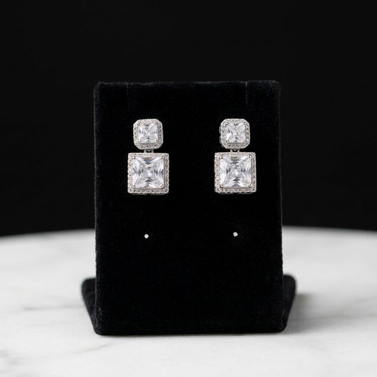 A refined sparkle shaped in perfect symmetry — the Pristelle Crystal Drops bring together modern geometry and timeless brilliance. Featuring radiant square-cut crystals framed with delicate halo detailing, these earrings capture light beautifully with every movement. Their elegant drop silhouette adds a graceful shimmer that elevates both everyday style and special occasion looks.