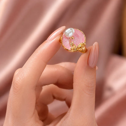 Like a delicate pearl resting within a blooming garden, this elegant ring captures a graceful blend of softness, nature, and feminine charm. Featuring a luminous pearl accent over a blush pink centerpiece with sculpted golden leaves, it creates a refined statement that feels romantic, artistic, and effortlessly luxurious.