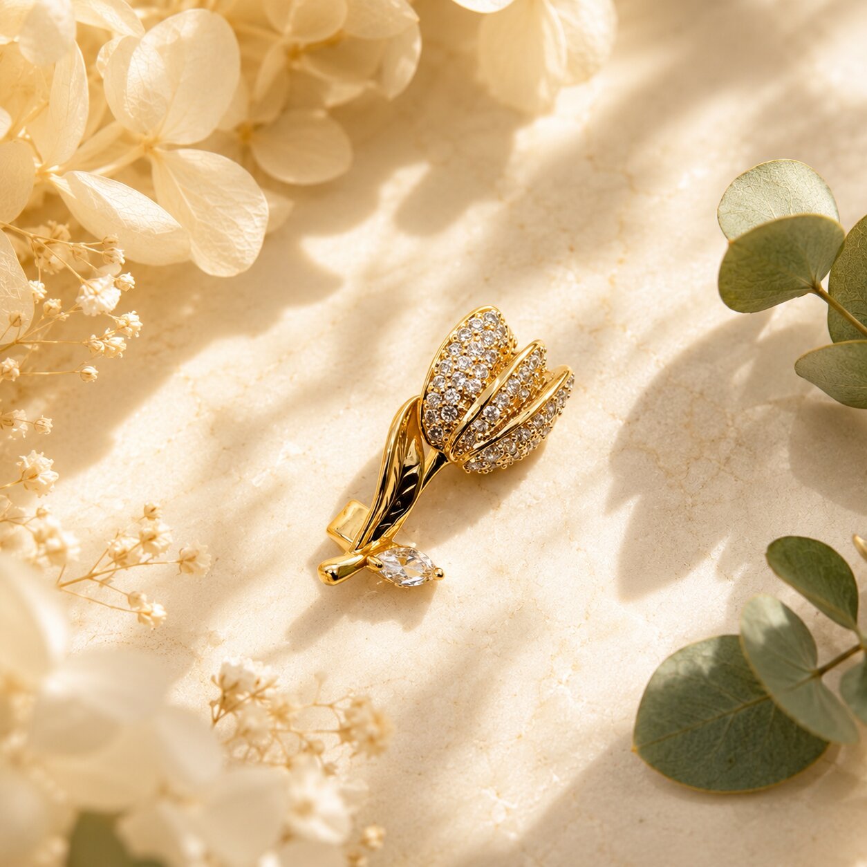 Like a golden tulip beginning to bloom beneath the morning light, this elegant brooch captures a beautiful sense of grace, renewal, and delicate femininity. Featuring crystal-studded petals paired with a polished sculpted stem and sparkling leaf accent, it creates a refined statement that feels radiant, romantic, and effortlessly luxurious.