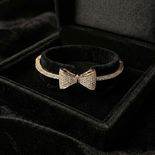 A delicate symbol of elegance and charm, this bow-inspired bracelet captures a soft sparkle that feels both graceful and modern. The sleek curve paired with shimmering stone detailing creates a refined look that effortlessly elevates everyday style.