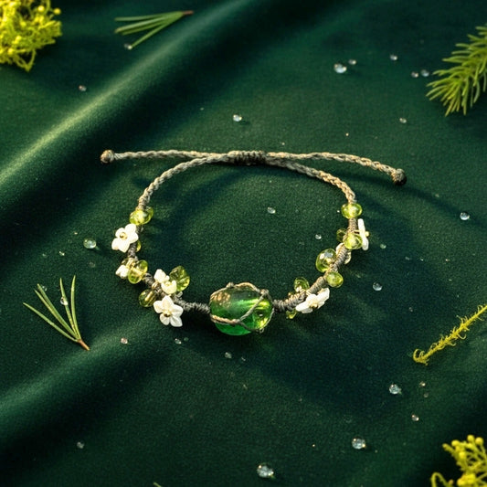 The Wild Ivy Twined Bracelet captures the earthy soul of nature with its handwoven macramé thread intertwined with green artificial crystals and tiny white lily blossoms.
